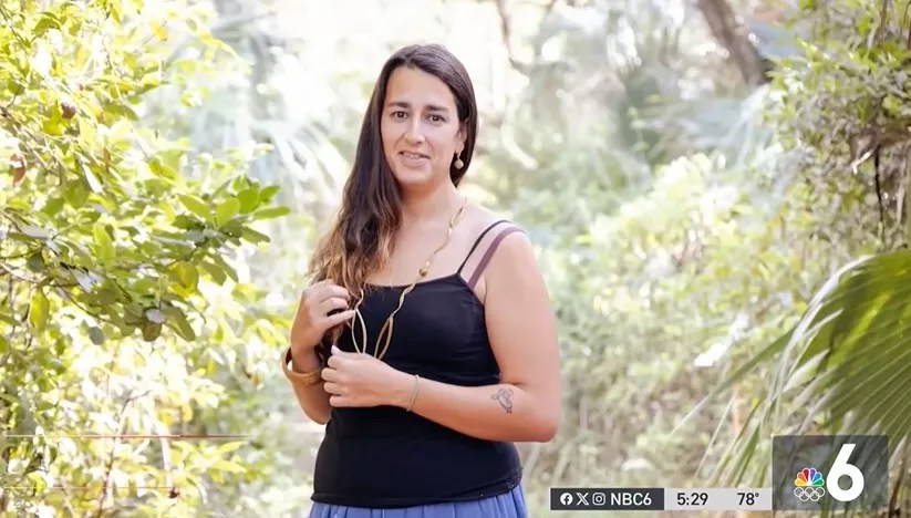 Andrea Dos Passos in a black tank-top standing in front of trees