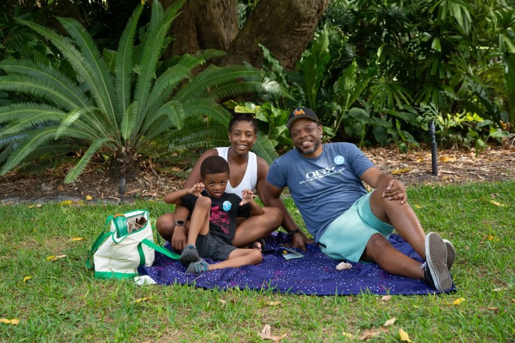 A mother and father with their child sitting on a picnic blanket at Fairchild Tropical Botanic Garden