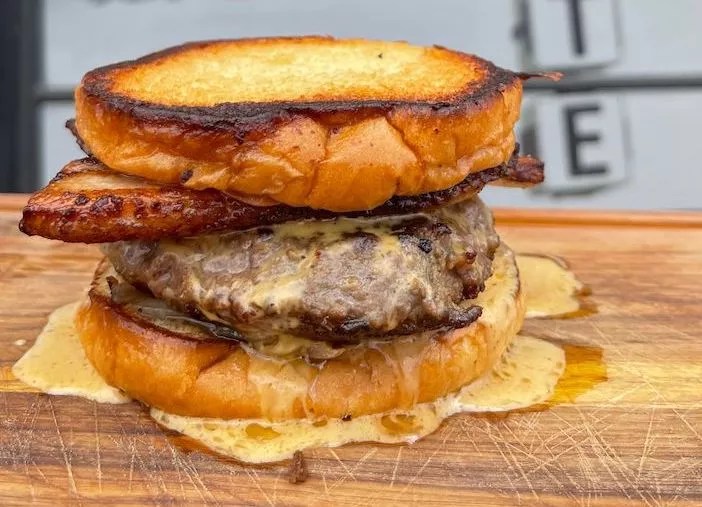 A burger with meat and cheese on a wooden serving platter