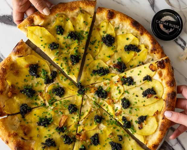 White pizza topped with caviar and a hand pulling it