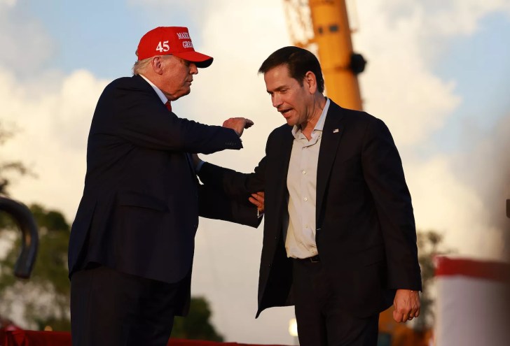Donald Trump, wearing a red MAGA hat, grasps Marco Rubio by the arm and pats him on the shoulder onstage in Miami.