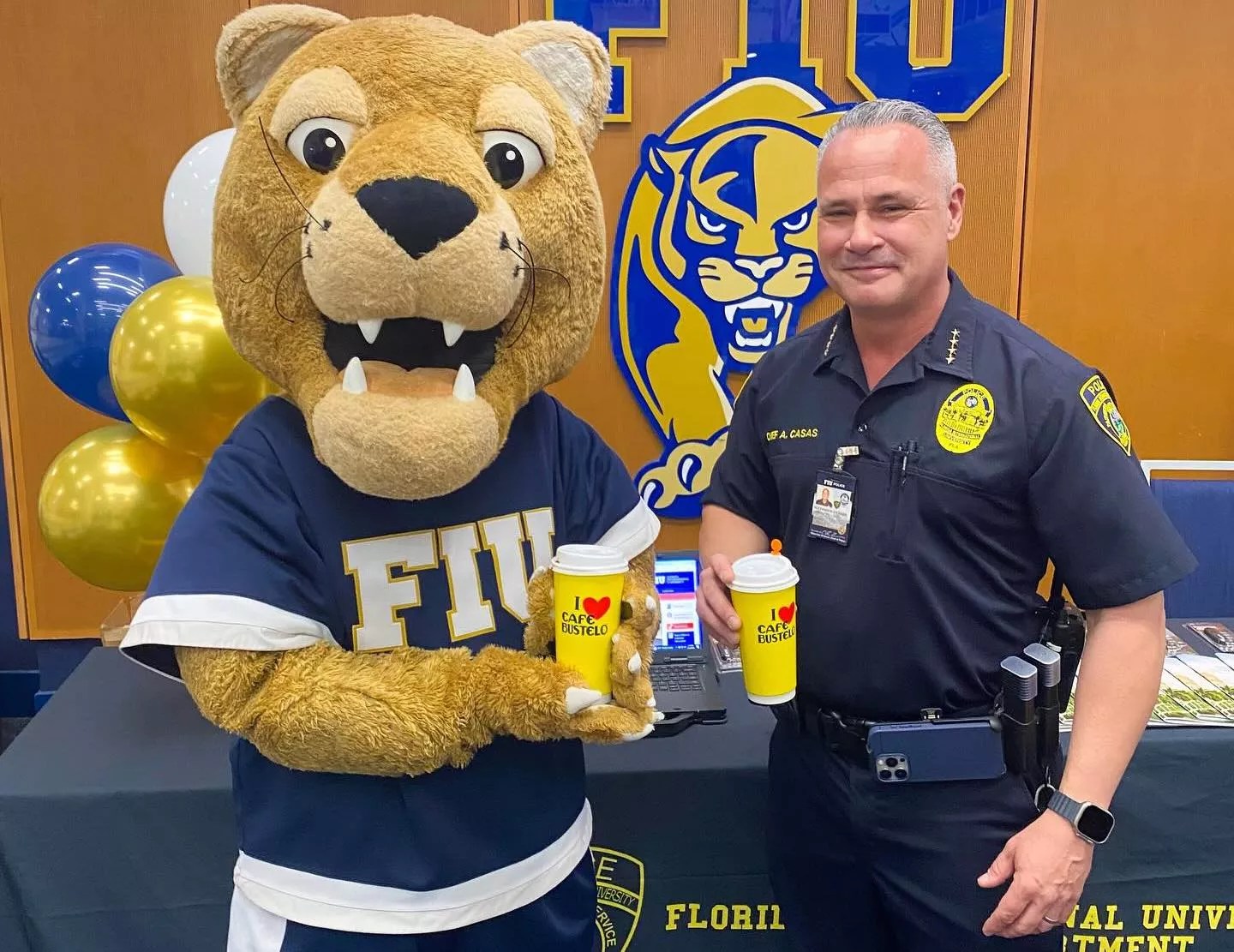photo of uniformed campus police chief posing with FIU panther mascot. Both are holding large branded Cafe Bustelo disposable coffee cups.