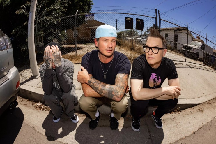 Photo of Blink-182 sitting on a curb.