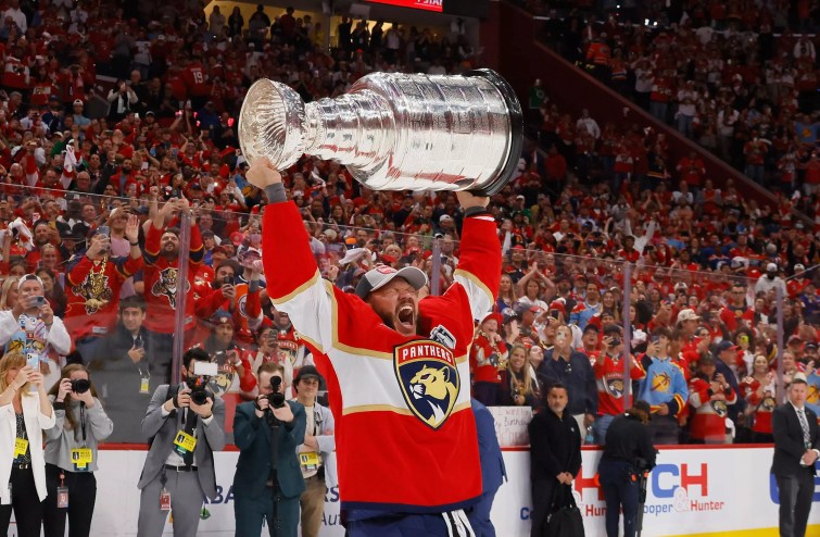 Panthers player Kyle Okposo lifts the Stanley Cup over his head on the ice in his home arena and yells out triumphantly