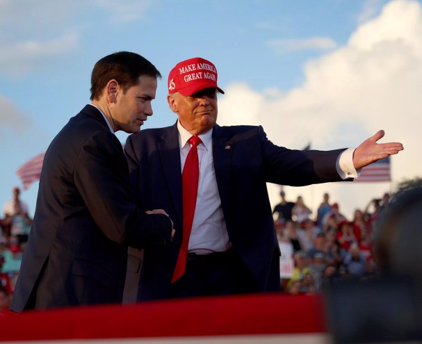 Donald Trump in a "Make America Great Again" cap shakes Marco Rubio's hand in front of a large crowd while directing him to the podium at a Miami-Dade rally