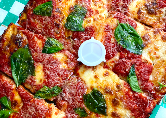 A close-up photo of a pizza from Old Greg's Pizza covered in cheese and basil