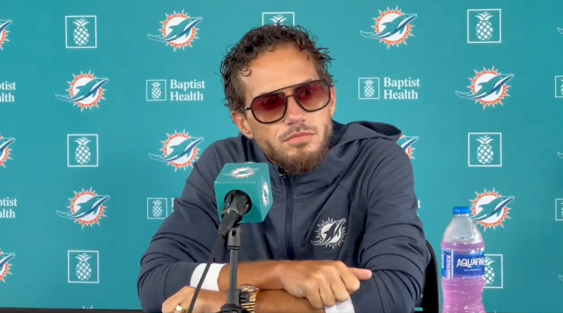 Mike McDaniel speaks at press conference with flashy shades, curly hair, and an overgrown beard.