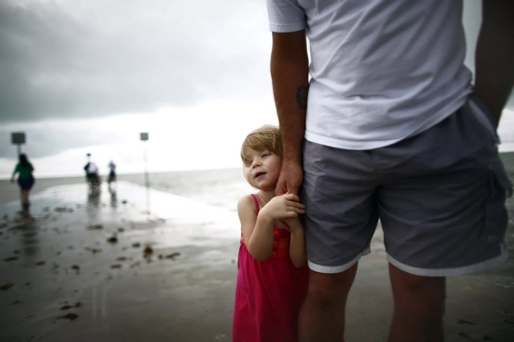 a small child in a red dress holding a man's hand on a beach in the Florida Keys on a stormy day