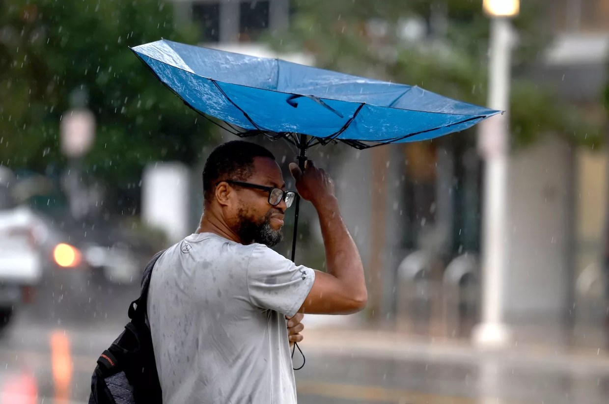 Wind blows a pedestrian's umbrella inside out as rain inundates the area on November 15, 2023, in Miami Beach, Florida, leaving Miami-Dade County soaked and causing concern for potential flooding.
