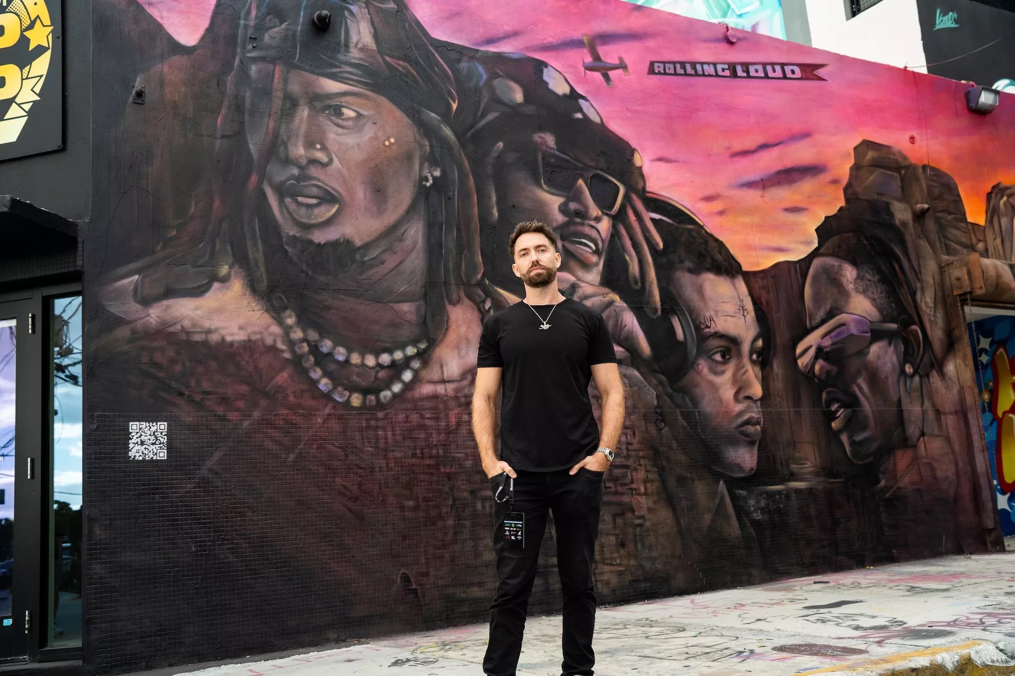 Rolling Loud co-founder Tariq Cherif standing in front of a mural of Future, Playboi Carti, Travis Scott, and XXXtentacion