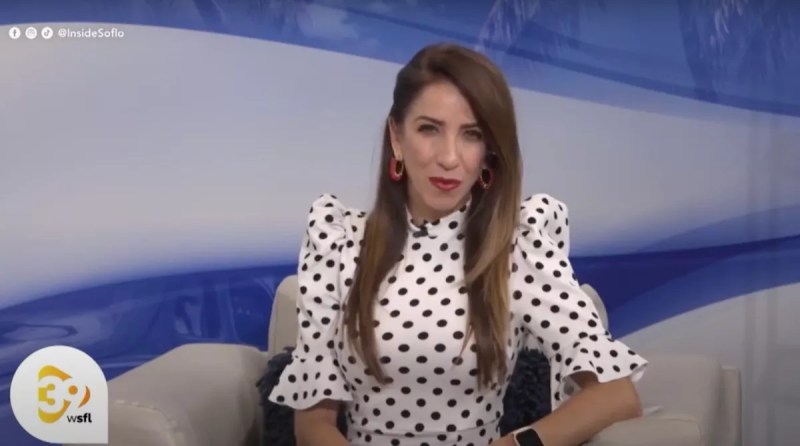 Ana Isabel Hume hosting Inside South Florida. She is sitting in a chair wearing a long sleeve white and black polka-dot dress. She is looking directly into the camera.