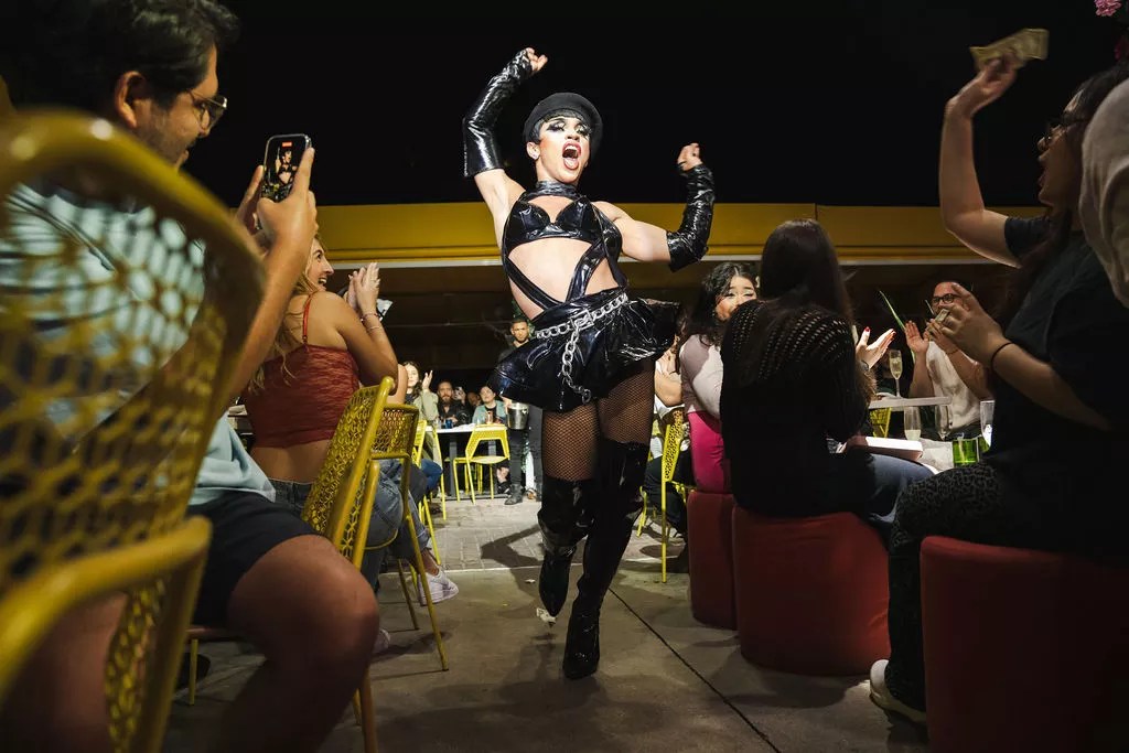 drag performer dressed in leather walks a runway between two seated crowds