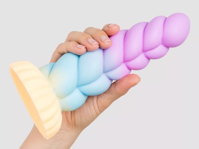 a hand holding a sex toy in the shape of a pastel rainbow-colored unicorn horn
