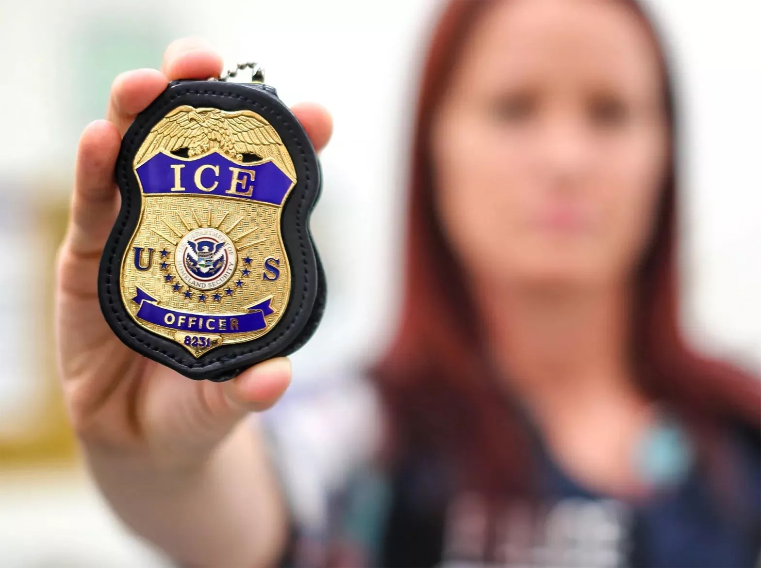 U.S. Immigration and Customs Enforcement photo of an agent, blurred in the background, brandishing an ICE badge