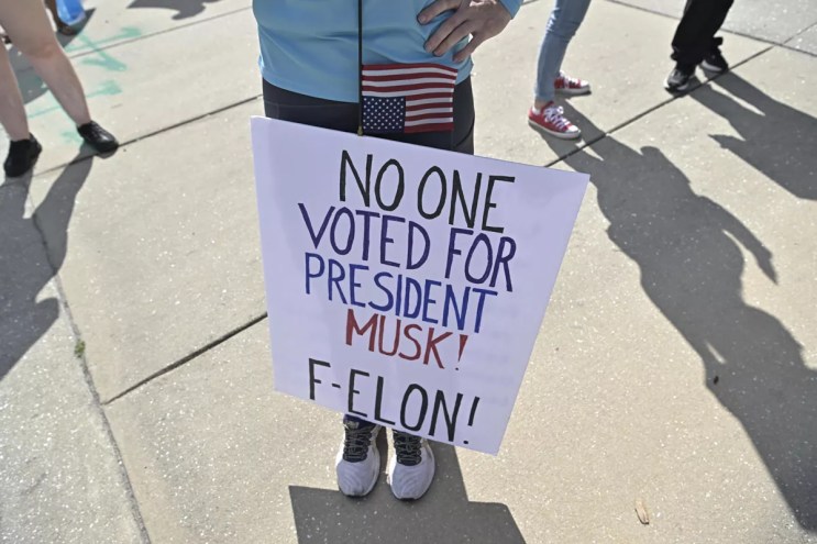 Someone holds a sign that reads, "No one voted for President Musk! F-ELON!"