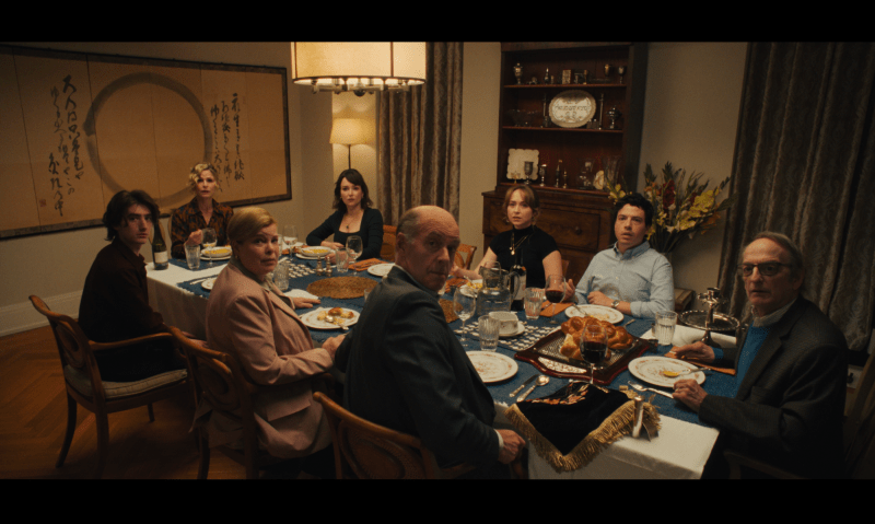 a film still of eight family members gathered around the dinner table glaring at the camera in unison