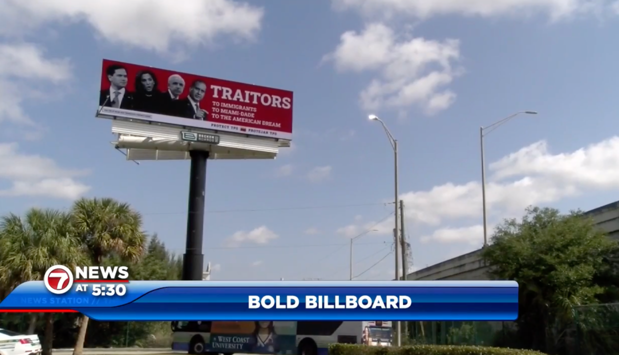A photo of a red billboard with four politicians on it and the words: “TRAITORS: To Immigrants, To Miami-Dade, To The American Dream” above a blue sky