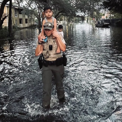 Florida Fish and Wildlife officer carries child on her shoulders through shin-deep water in a flooded street