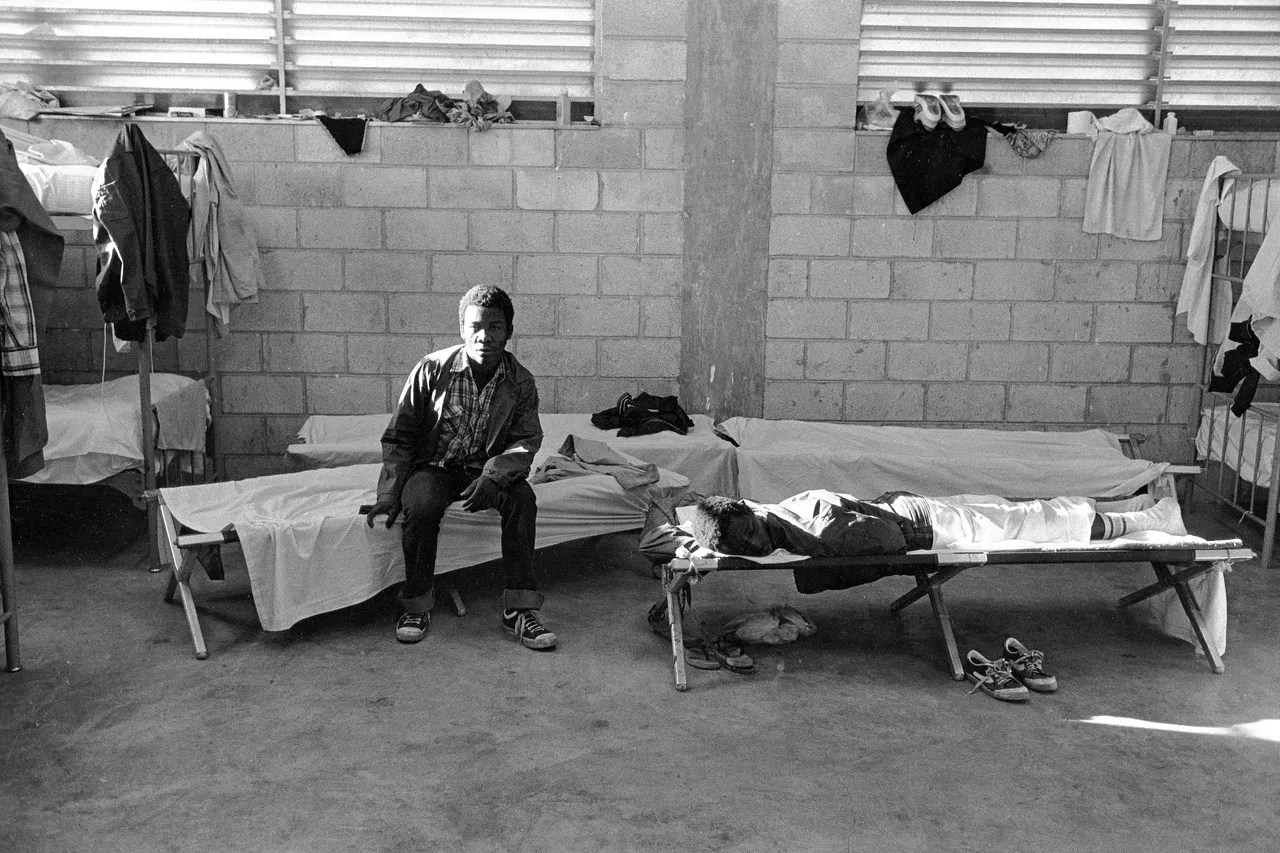 Two men sitting on beds inside what was then known as the INS Krome Detention Camp.