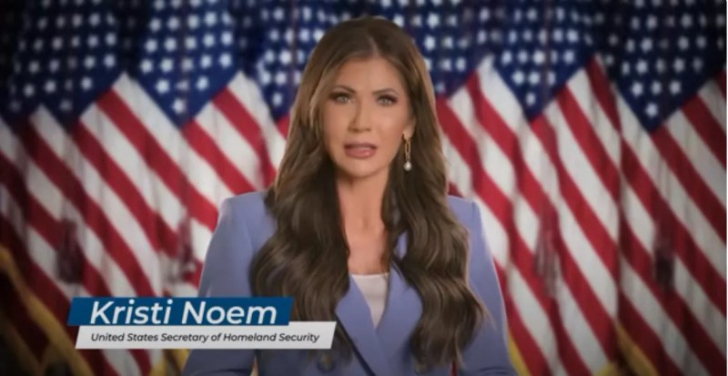 Kristi Noem speaking to the camera with American Flags in the background