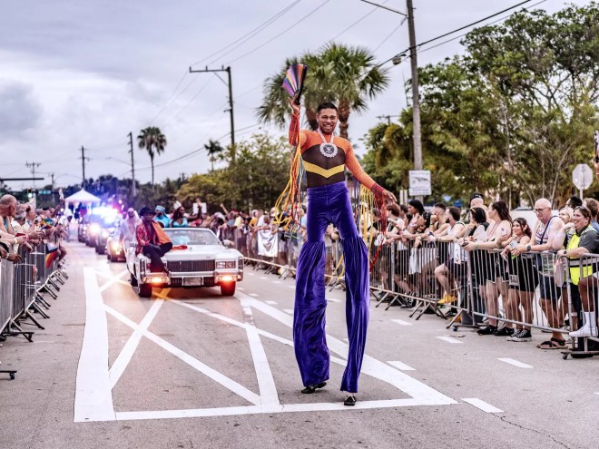a man on stilts leads a parade route