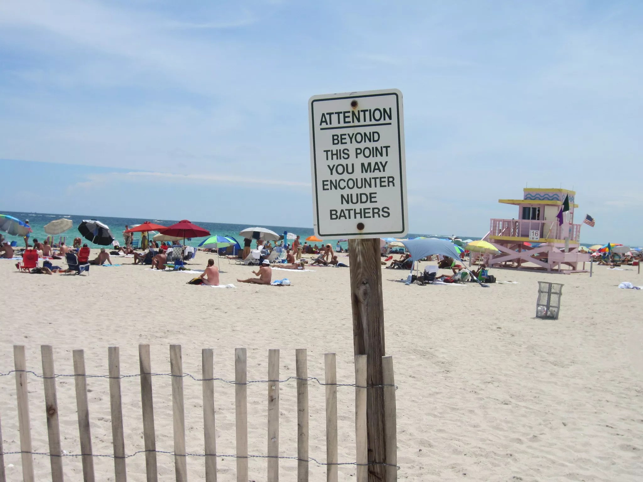 A sign leading to a sandy Miami beach that reads, in all uppercase letters: Attention: Beyond this point you may encounter nude bathers
