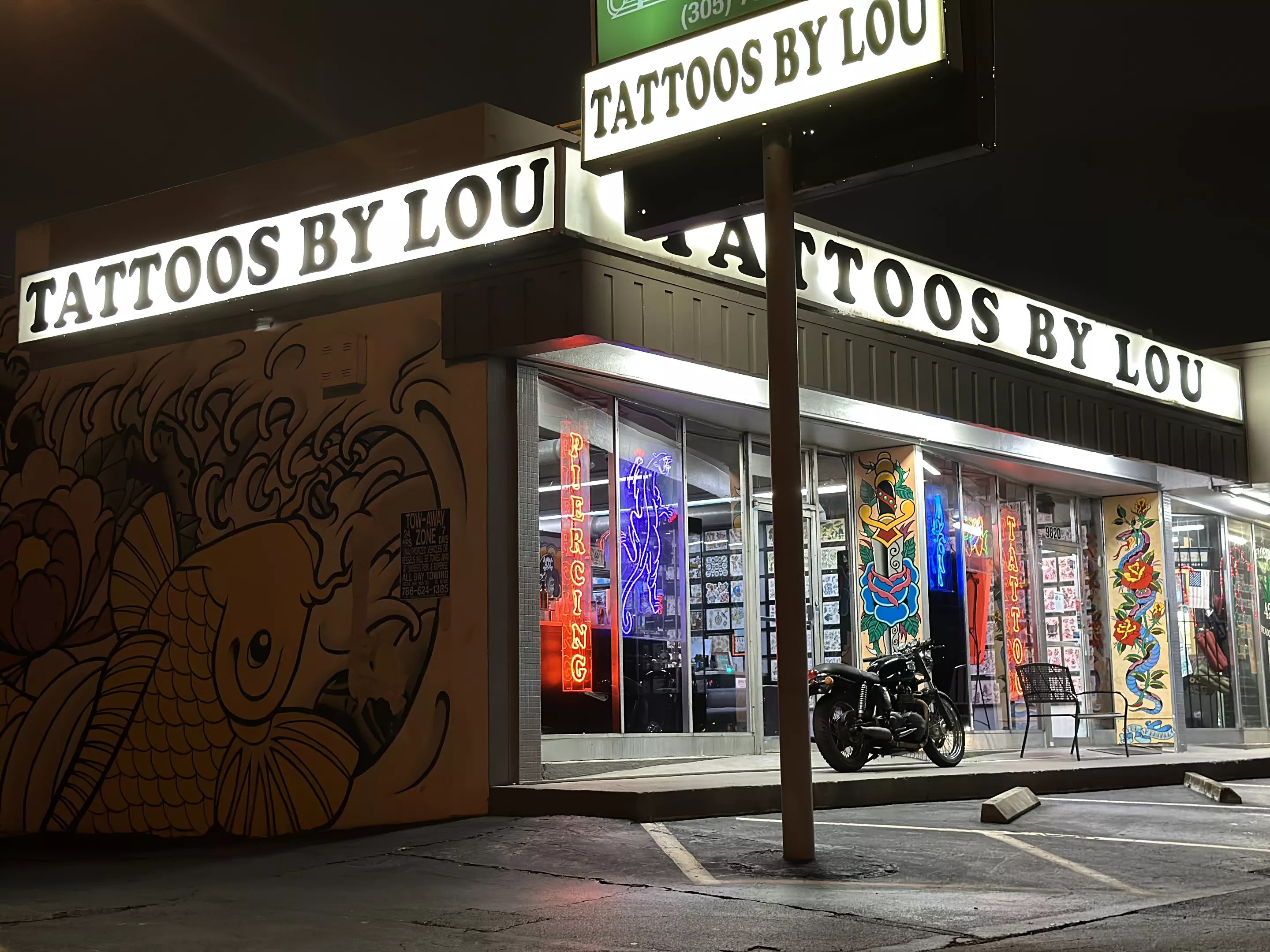 facade of a tattoo shop with three marquees reading "Tattoos By Lou"