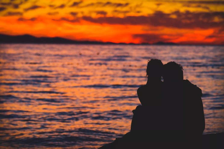 a couple in silhouette looks out at the ocean during golden hour