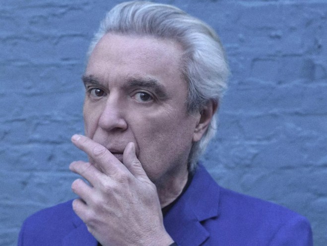 cyan-tinged headshot of David Byrne, with his gray hair swept back and his left hand partially covering his mouth, as if stifling a cough