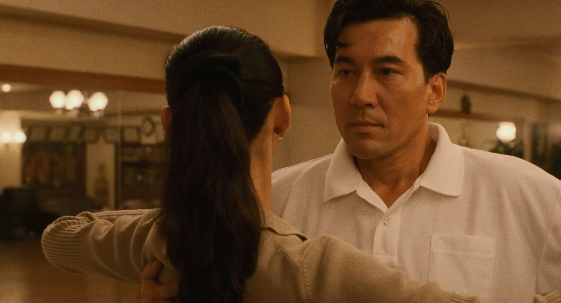 film still from Masayuki Suo's <i>Shall We Dance?</i> shows a closeup of actor Kōji Yakusho speaking to a woman with her back to the viewer