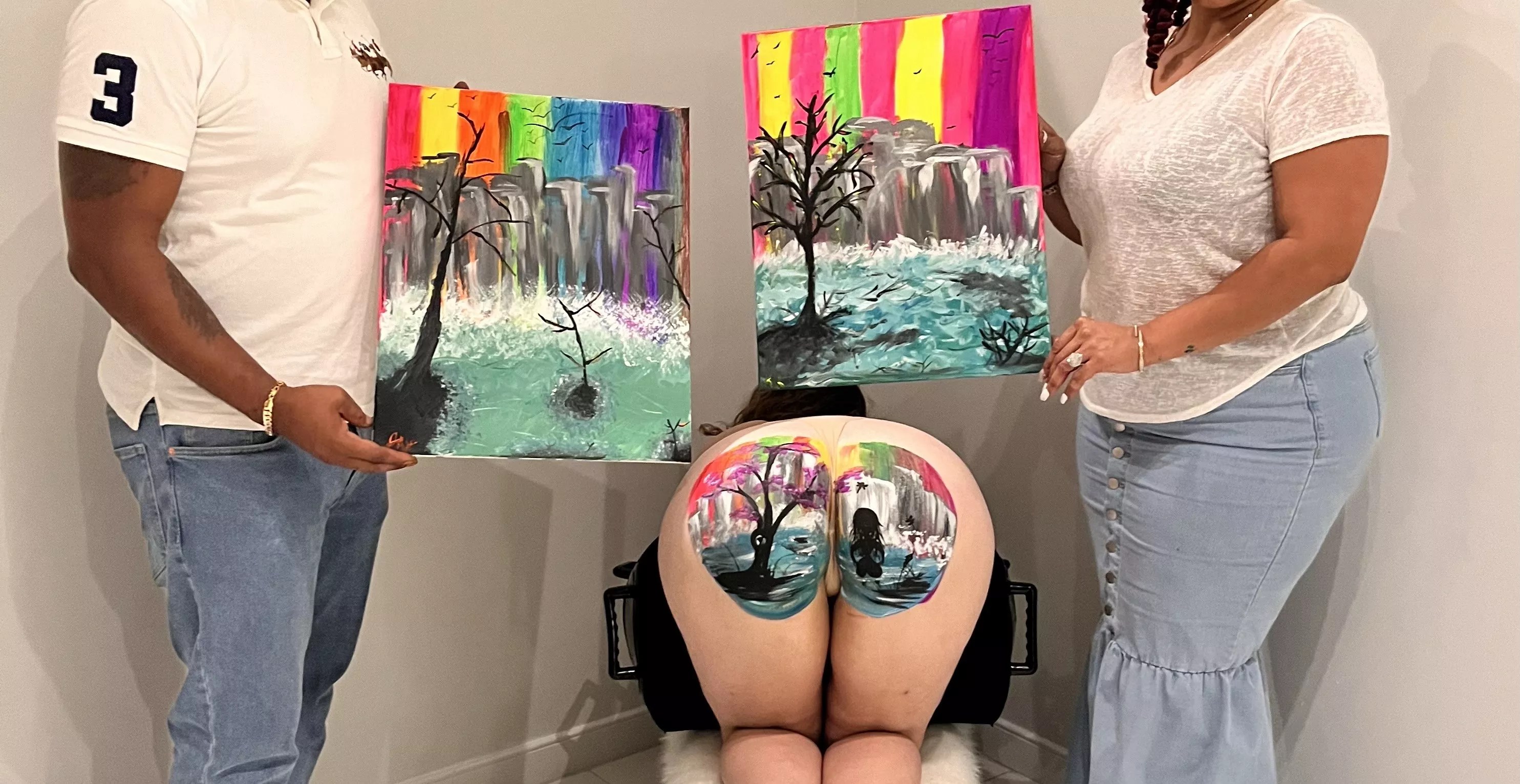 two people hold canvases depicting landscapes on either side of a model's butt depicting a similar landscape