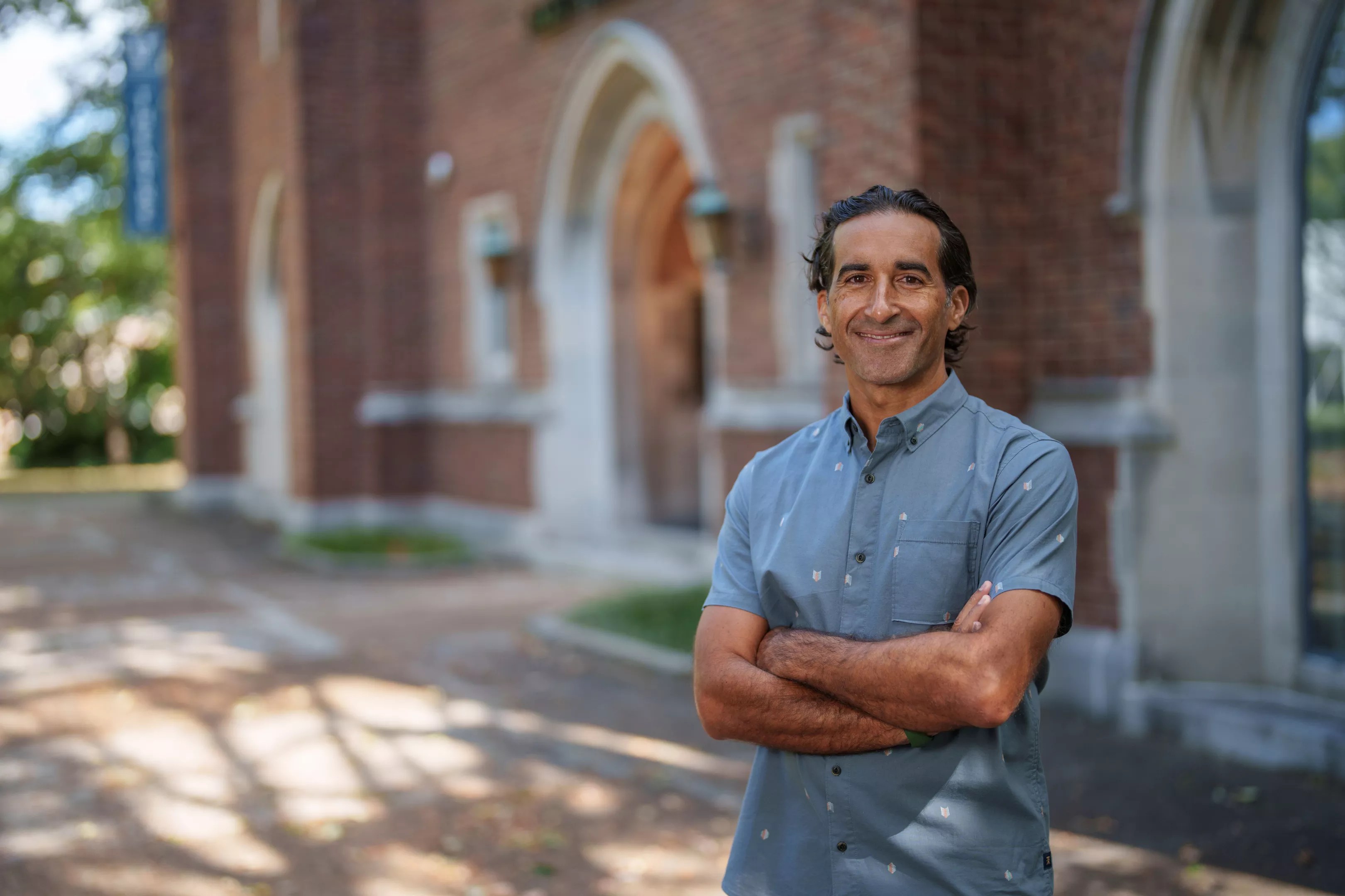 Portrait of a man in a button-down blue shirt standing in front of a brick building