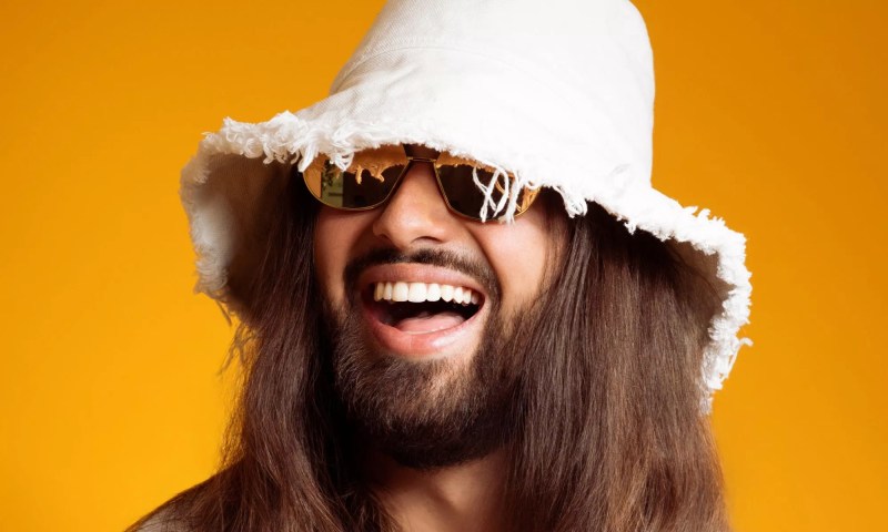 Picture of a man with long hair wearing a white hat against a yellow background.