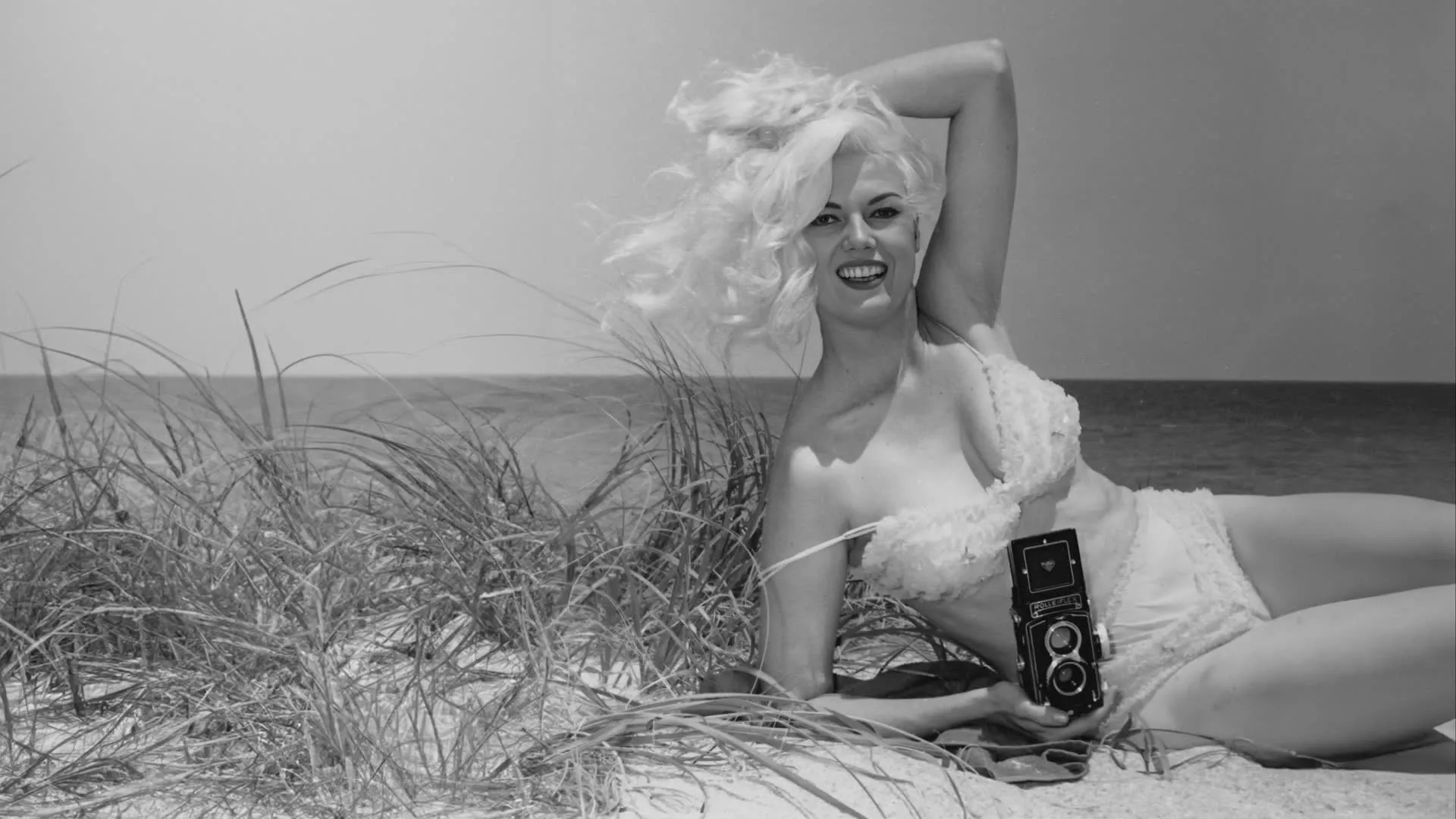 a black-and-white photo of a woman on the beach in her bikini in the '50s