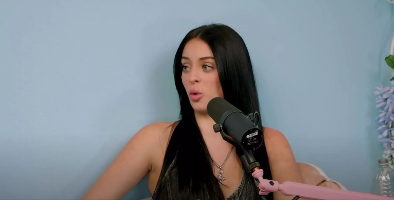 a woman sits in front of a microphone to record a podcast