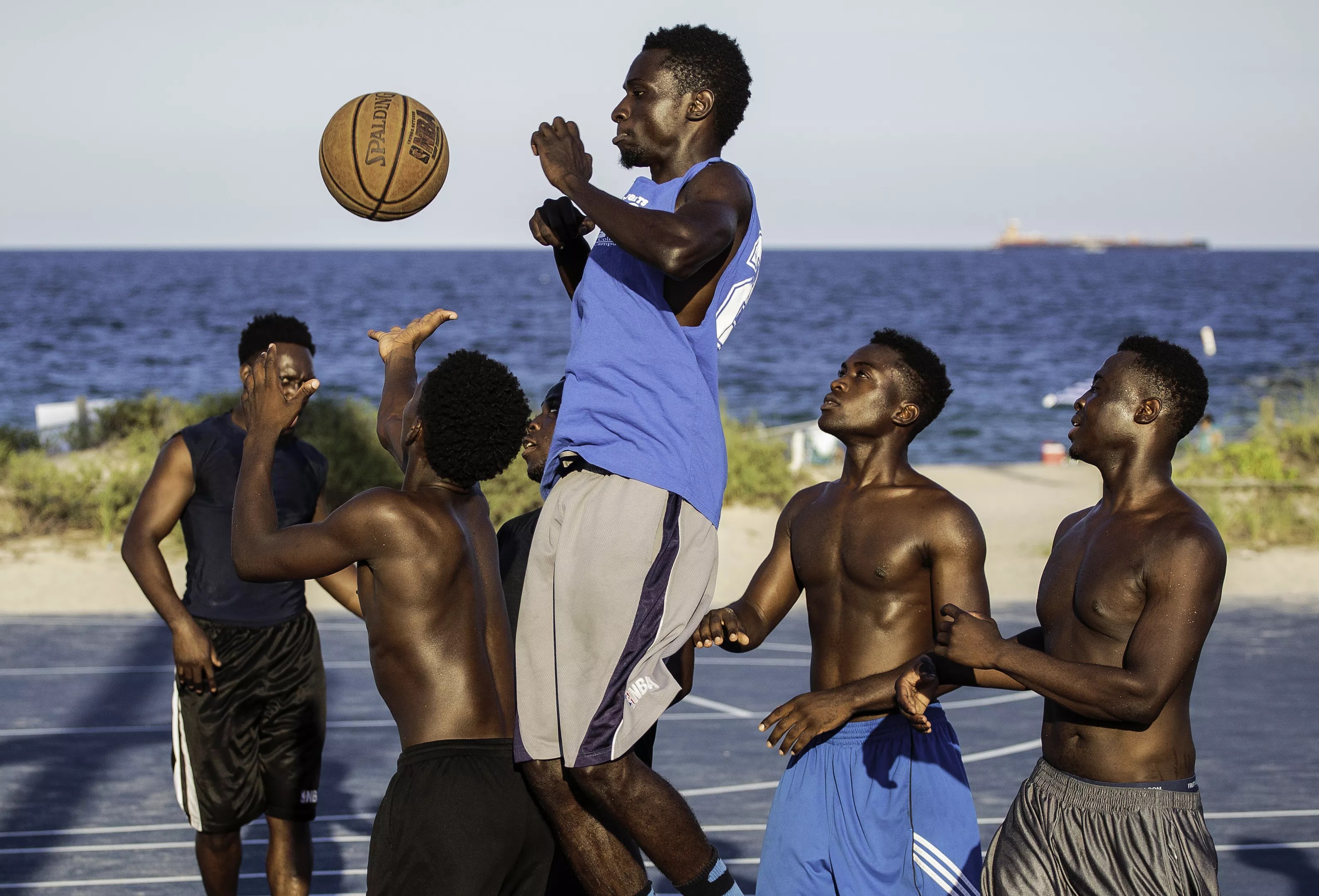 Depicted are men playing basketball at a popular beachside court in Fort Lauderdale.