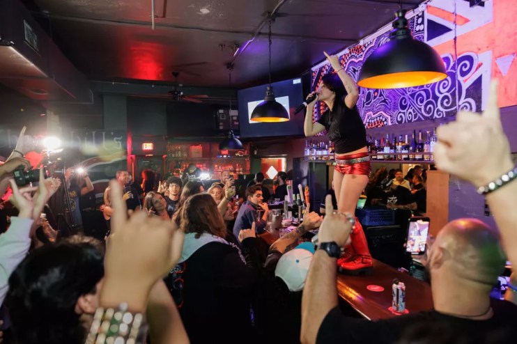 A woman singing on top of a bar surrounded by people.