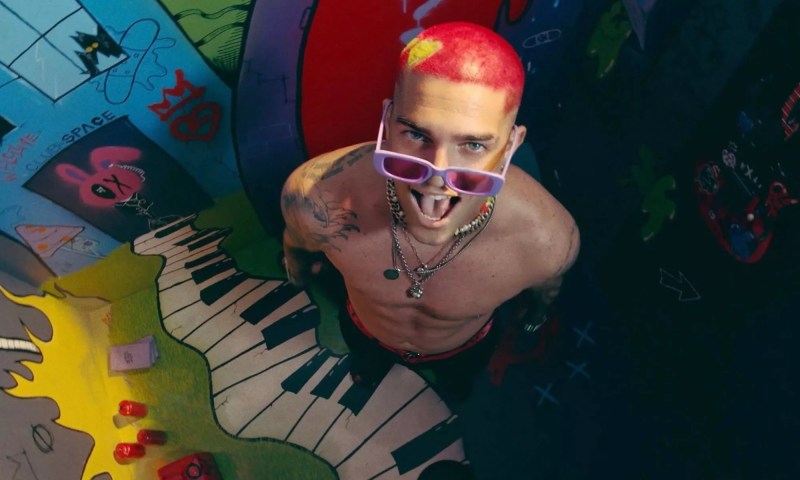 Picture of a man with red hair and tattoos standing in front of a mural.