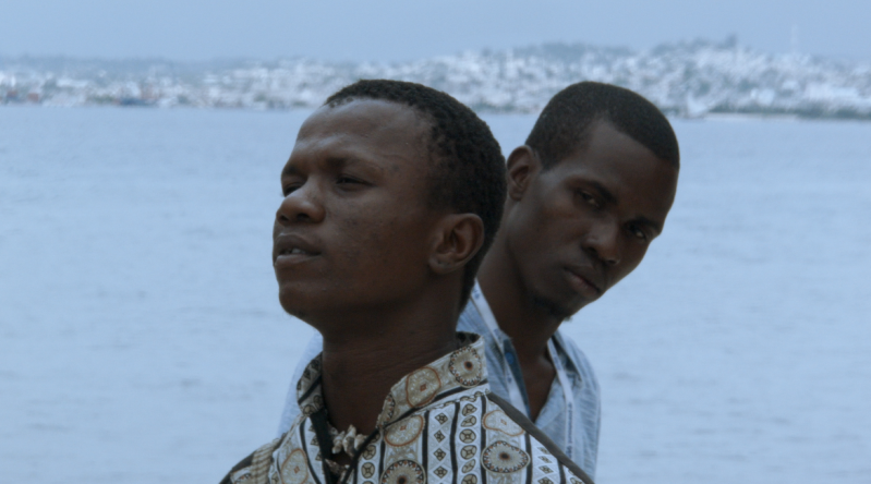 a still from a film showing a close-up of a Black man standing behind another