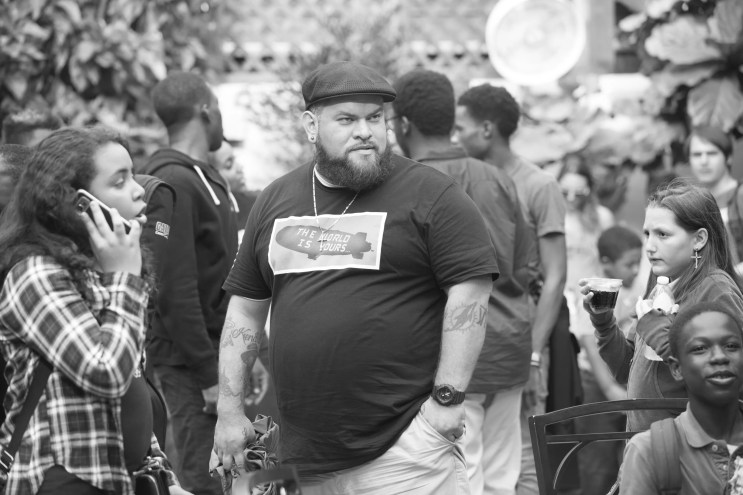 Black and white picture of a man with tattoos wearing a hat.