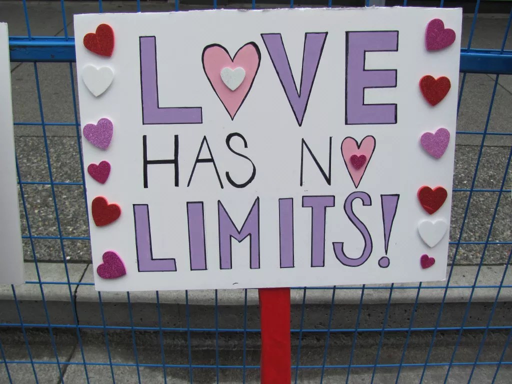 a painted protest sign with heart stickers reads, "Love has no limits!"
